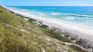 A beach with a sandy shore, a wooden fence, and a grassy hill. - Adagio A101 | Private Beach | Ground Floor Unit | 2 pools | Bonus Bunk Room!! (Santa Rosa Beach)