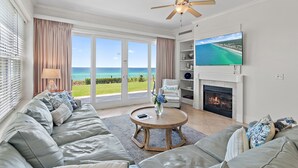A living room with a sofa, a coffee table, a fireplace, a TV, and a view of the ocean. - Adagio A101 | Private Beach | Ground Floor Unit | 2 pools | Bonus Bunk Room!! (Santa Rosa Beach)