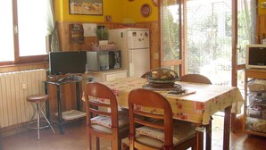 A dining area with a table set for four, wooden chairs, a television on a stand, and a refrigerator in the background. - House Yanina (Bellano)