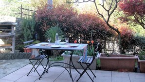 An outdoor patio with a table set for two, surrounded by potted plants and trees. - House Yanina (Bellano)