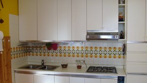 A kitchen with white cabinets, a gas stove, a sink, and a decorative backsplash. - House Yanina (Bellano)