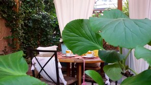A small outdoor seating area with a table and chairs, surrounded by lush greenery.
