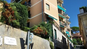 A multi-story residential building with balconies, a stone wall with a sign, and lush greenery.