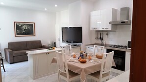 A modern kitchen with white cabinets, a dining area with a table set for four, and a grey sofa in the living area. - Casa Vicki (Genoa)