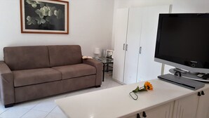 A modern living room with a brown sofa, a flat-screen TV, a white table, and a framed abstract painting. - Casa Vicki (Genoa)