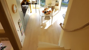 A staircase leading to a dining area with a table set for two, a kitchen in the background, and a view of the outdoors.