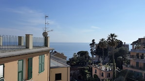 A coastal residential area with a view of the sea, featuring buildings with balconies and green shutters.