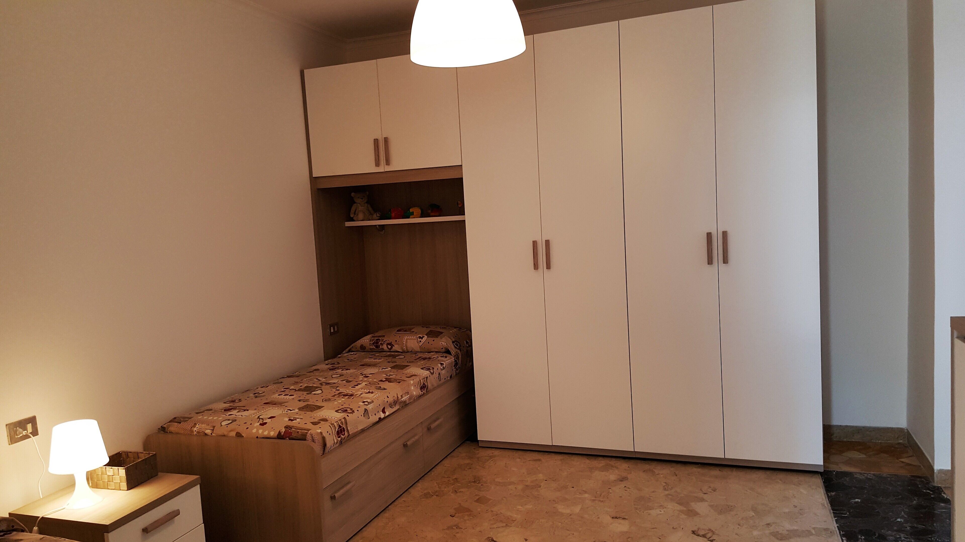 Un dormitorio con una cama, un escritorio con lámpara y un armario.