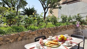 An outdoor dining area with a stone wall, a table set with plates of food, cups, and a teapot. - Casa Agrumeto (Genoa)