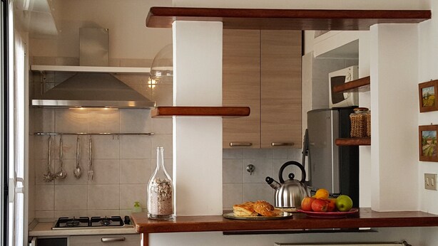 A modern kitchen with a gas stove, stainless steel kettle, and a fruit bowl on the counter. - Casa Agrumeto (Genoa)
