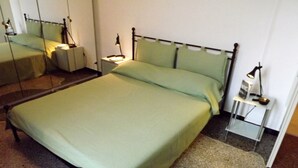 Un lit bien fait, avec une couverture verte et des oreillers, une table de chevet avec une lampe et une petite table de nuit.