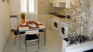 Une cuisine compacte comprenant une table à manger, des chaises, un réfrigérateur, un lave-linge et un panneau de verre décoratif.