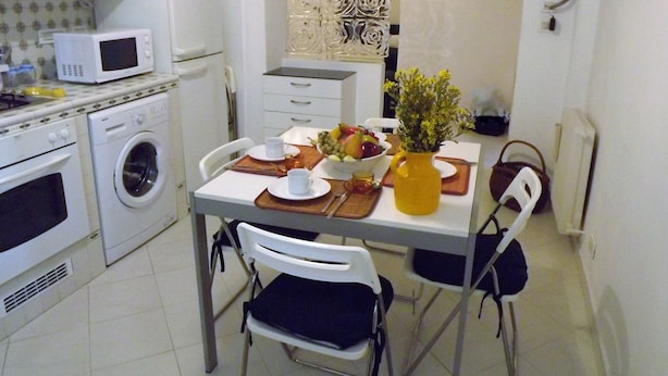 Une cuisine compacte équipée d’un four à micro-ondes, d’un lave-linge et d’un coin repas avec des chaises et une table pour deux personnes.