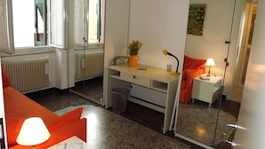Une chambre d’hôtel compacte comprenant un coin cuisine, un petit bureau, une chaise, un canapé, un miroir et une fenêtre.