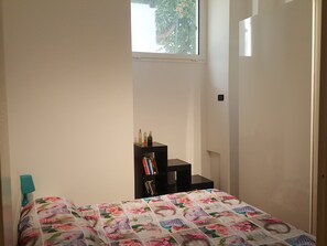 Un dormitorio con cama, ventana, estantería y puerta.