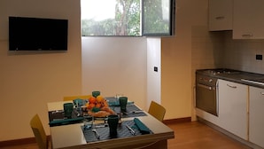 A dining area with a table set for two, a window with a view of greenery, and a kitchen with modern appliances. - House Sole (Genoa)
