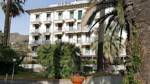 A multi-story building with balconies, surrounded by lush greenery and palm trees. - House Sole (Genoa)