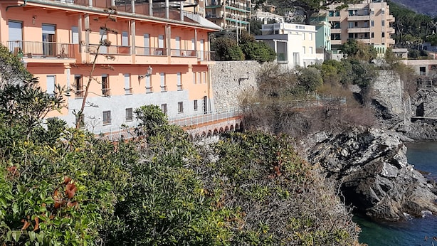 A coastal town with multi-story buildings, a stone wall, and rocky cliffs. - House Betta (Genoa)