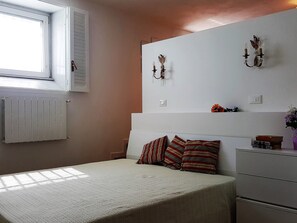 Une chambre à coucher avec un lit, un radiateur, une fenêtre et un luminaire fixé au mur.
