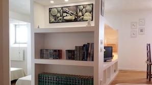 A room with a bookshelf containing books and decorative items, a bed, a window, and a lamp. - House Betta (Genoa)