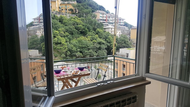 A balcony with a table set for breakfast, overlooking a hillside with buildings. - Casa Barbara (Bogliasco)