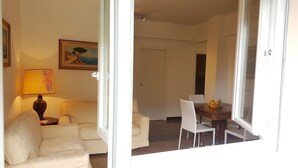 A living room with a sofa, a table with chairs, a lamp, and a painting on the wall. - Casa Barbara (Bogliasco)