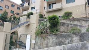 A residential building with multiple balconies, a staircase, and a concrete retaining wall with vegetation. - Casa Barbara (Bogliasco)