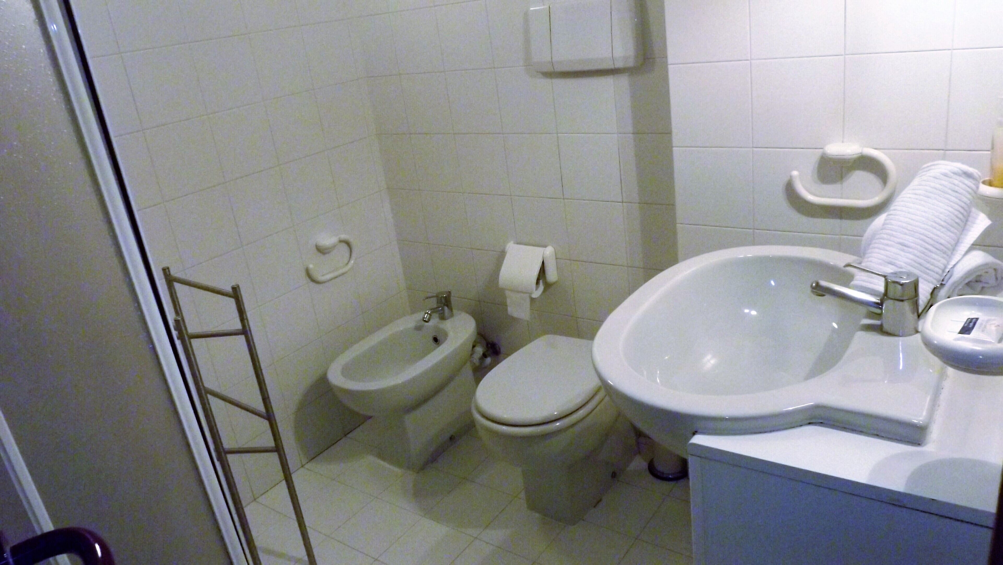 A bathroom with a bidet, toilet, sink, and towel rack.