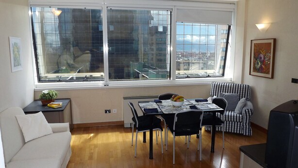 A dining area with a table set for two, a striped armchair, a sofa, and a TV. - House Asfodelo (Genoa)