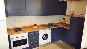 A compact kitchen with a washing machine, a sink, and a small countertop with a bowl of fruit. - House Asfodelo (Genoa)