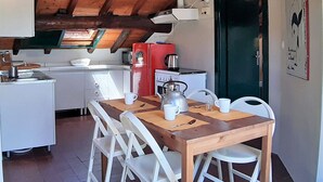 A compact kitchen with a wooden ceiling, a red refrigerator, a stove, and a microwave. There is a dining table with chairs and a coffee pot on it. - Sea Attic (Noli)