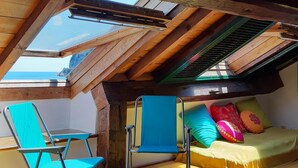 A cozy attic bedroom with a skylight, a bed with colorful pillows, and a blue chair. - Sea Attic (Noli)
