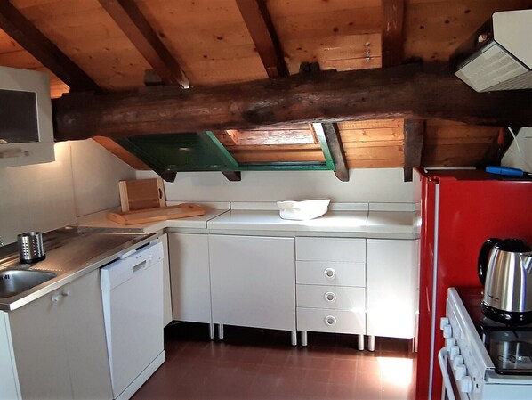 A compact kitchen with white cabinets, a red refrigerator, and a wooden ceiling.