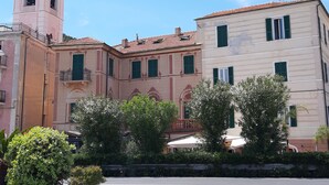 A historic building with a bell tower, green shutters, and a courtyard with trees and outdoor seating. - Sea Attic (Noli)