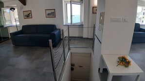 A living room with a blue sofa, a staircase with a metal railing, and a view of the sea through a window. - La Torre (Bogliasco)