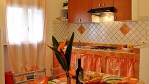 Un comedor con una mesa preparada para dos, una cocina al fondo y una ventana con cortinas.