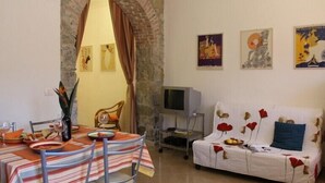 Un área de comedor con una mesa dispuesta para dos personas, un sofá con tapicería floral y un televisor sobre un mueble bajo.
