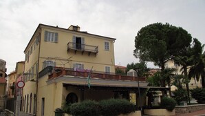 A yellow building with a balcony, a trash bin, and a street in front. - Azzurro Pervinca (Finale Ligure)