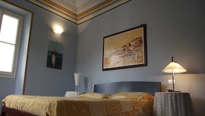 A bedroom with a bed, a nightstand, a table with a lamp, and two paintings on the wall. - Azzurro Pervinca (Finale Ligure)
