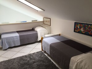 A small, clean room with two single beds, a window with a view, a framed picture on the wall, and a tiled floor. - Casa Azalea (Sanremo)