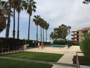 A pool area with palm trees, a building with balconies, and a grassy lawn. - Casa Azalea (Sanremo)
