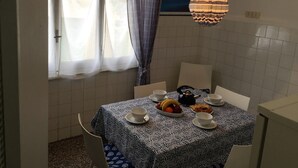 A dining area with a table set for two, a window with curtains, and a wall-mounted light fixture. - Casa Mon Amour (Moneglia)
