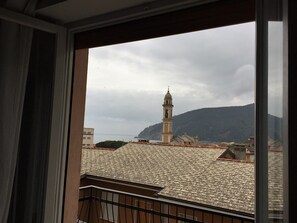 Vista de un pueblo costero con una torre del reloj destacada y una montaña al fondo.