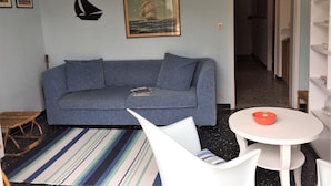 A living room with a blue sofa, a striped rug, a white table with a red bowl, and a framed picture of a sailing ship. - Casa Mon Amour (Moneglia)