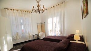 A hotel room with two beds, a chandelier, a desk, and a chair. - House Bella (Arenzano)
