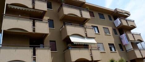 Un edificio residencial de varios pisos con balcones, algunos con toldos, y una bicicleta estacionada adelante.