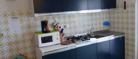 Cocina compacta con microondas, estufa y lavamanos. Hay armarios sobre la encimera y una mesita con un juguete.