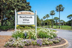 A sign for Beachside Beachwalk Villas with a landscaped garden and palm trees.