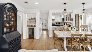 Una cocina amplia con armarios blancos, un comedor con mesa de madera y sillas de mimbre, y un aparador negro con puertas de vidrio.
