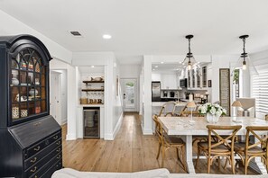 Une cuisine spacieuse avec des meubles blancs, un coin repas comprenant une table en bois et des chaises en osier, ainsi qu’une armoire noire aux portes en verre.